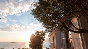 Un bâtiment situé sur la côte, doté d’un balcon donnant sur la mer, avec un arbre au premier plan et un ciel dégagé.