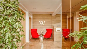 A reception area with a wooden wall, two red chairs, a reception desk, and a potted plant. - Maison W (Kotor)