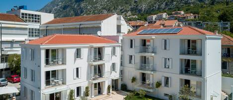 Un moderno edificio de apartamentos con balcones, piscina y montañas al fondo.