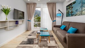 A modern living room with a sofa, a TV, a coffee table, and a view of the outdoors. - Maison W (Kotor)