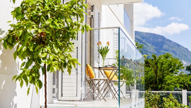 A balcony with a glass railing, a chair, and a yellow cushion. - Maison W (Kotor)