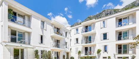 A modern multi-story residential building with balconies, a courtyard, and a mountainous backdrop.