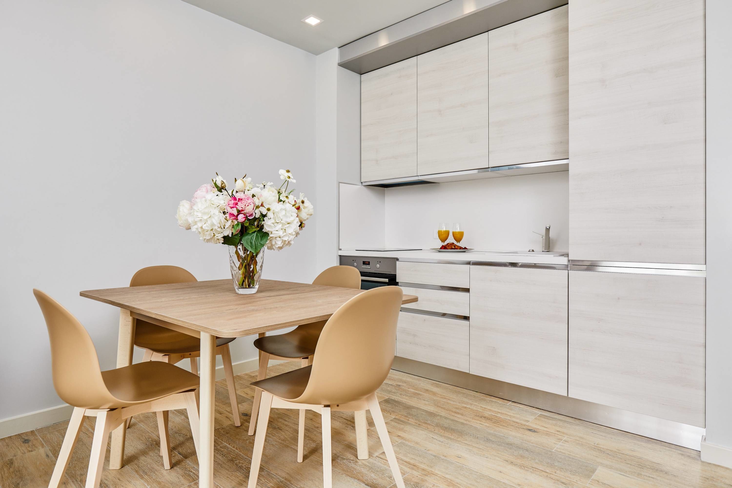 A modern kitchen with a wooden table and chairs, a vase of flowers, and stainless steel appliances.