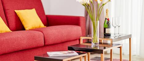 A modern living room with a red sofa, yellow pillows, a glass vase with flowers, a bottle of champagne, and two glasses on a wooden coffee table.
