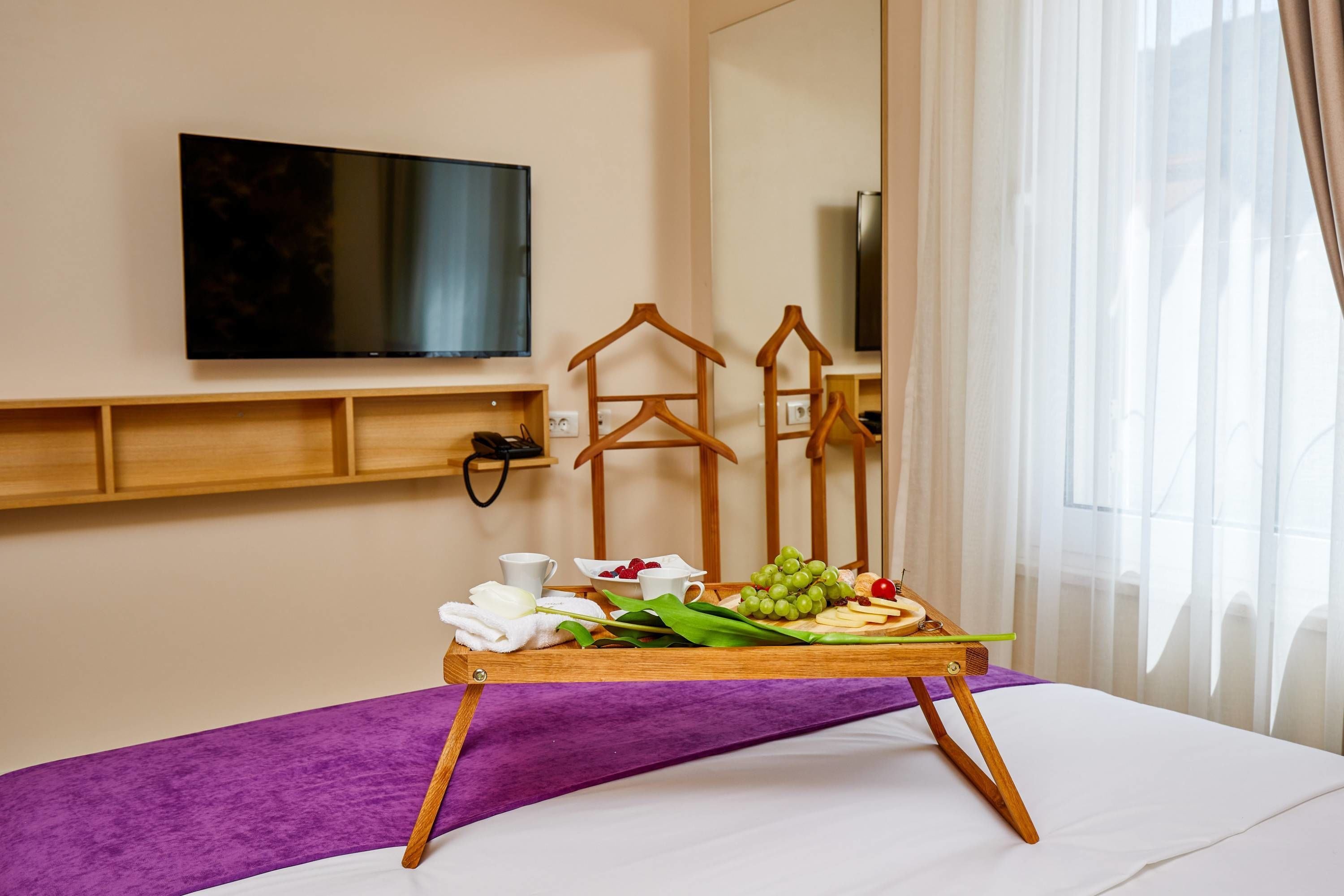 A hotel room with a bed, a tray with snacks, a TV, and a mirror.