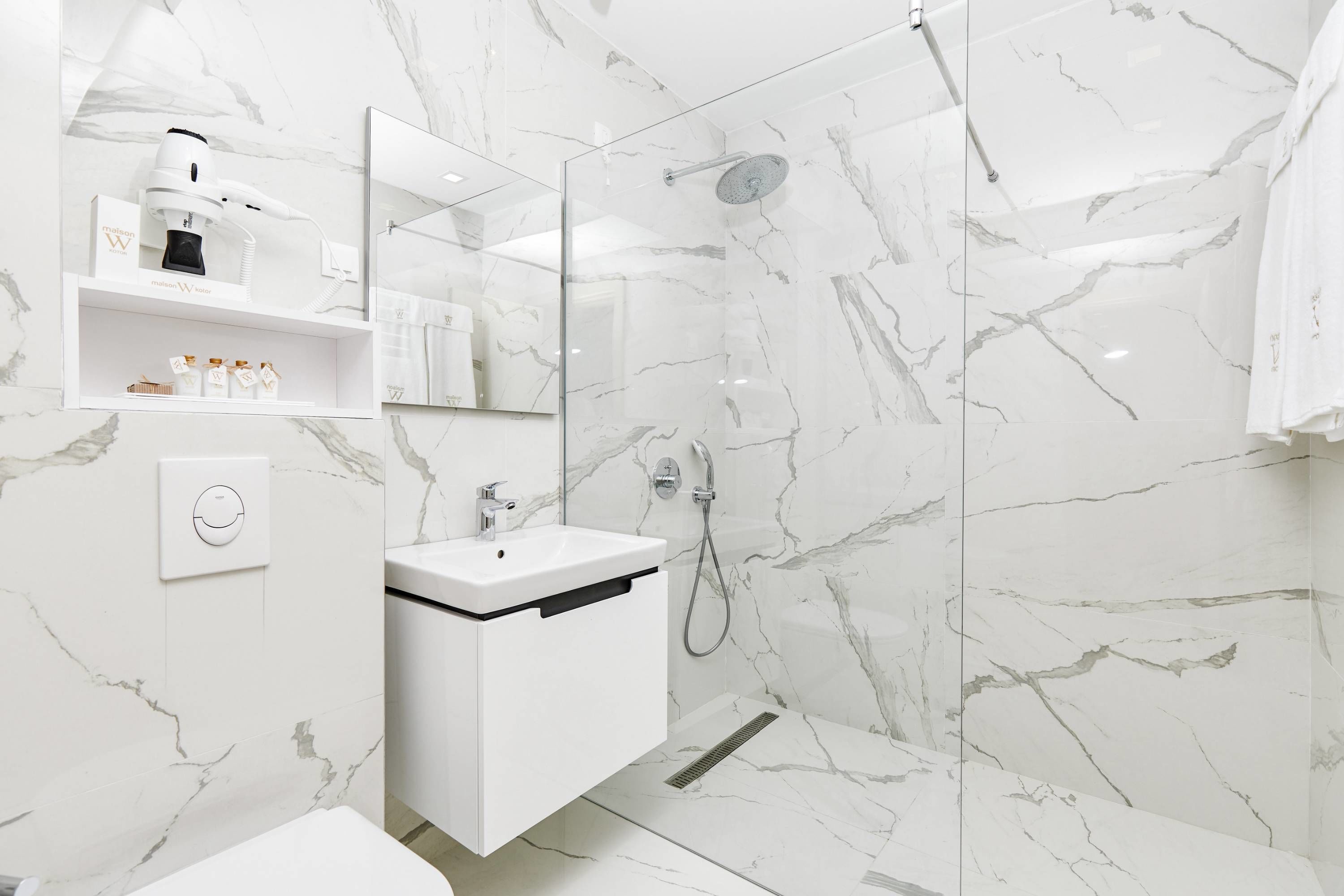 A modern bathroom with a white marble sink, a hairdryer on a shelf, and a glass-enclosed shower.