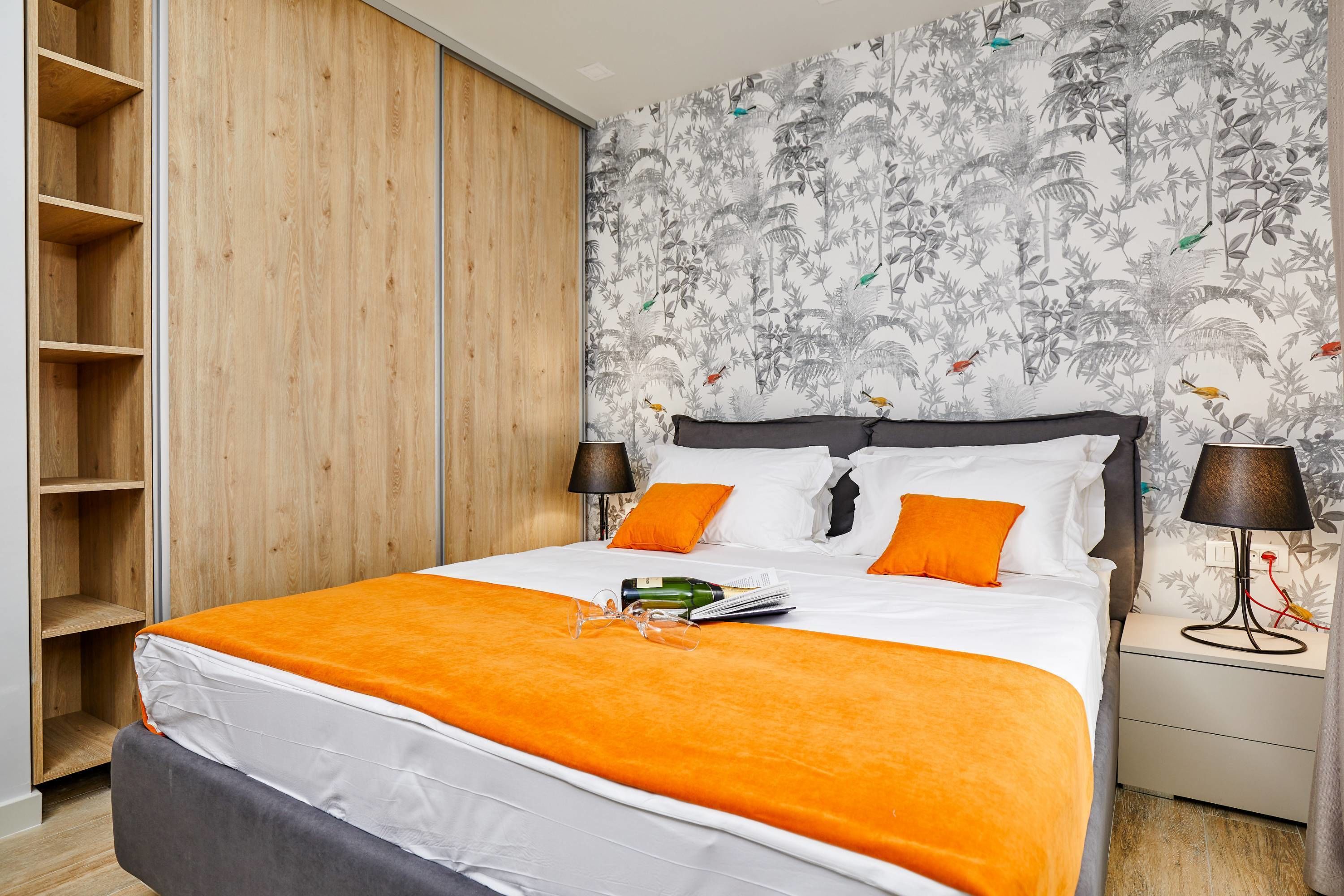 Een hotelkamer met een bed, nachtkastje, lamp en garderobe.