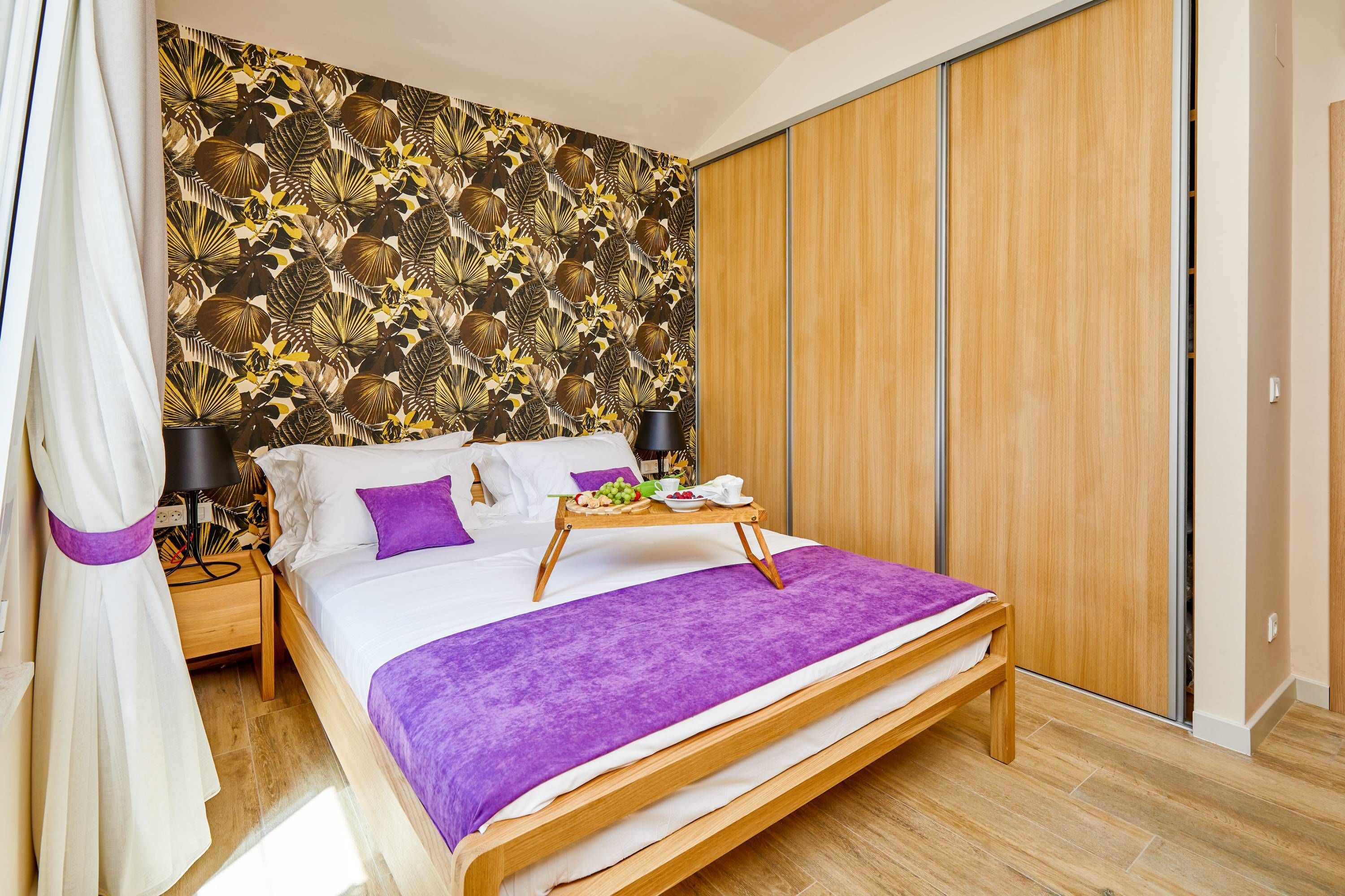 A bedroom with a bed, a tray with fruits, a nightstand, a lamp, and a wardrobe.