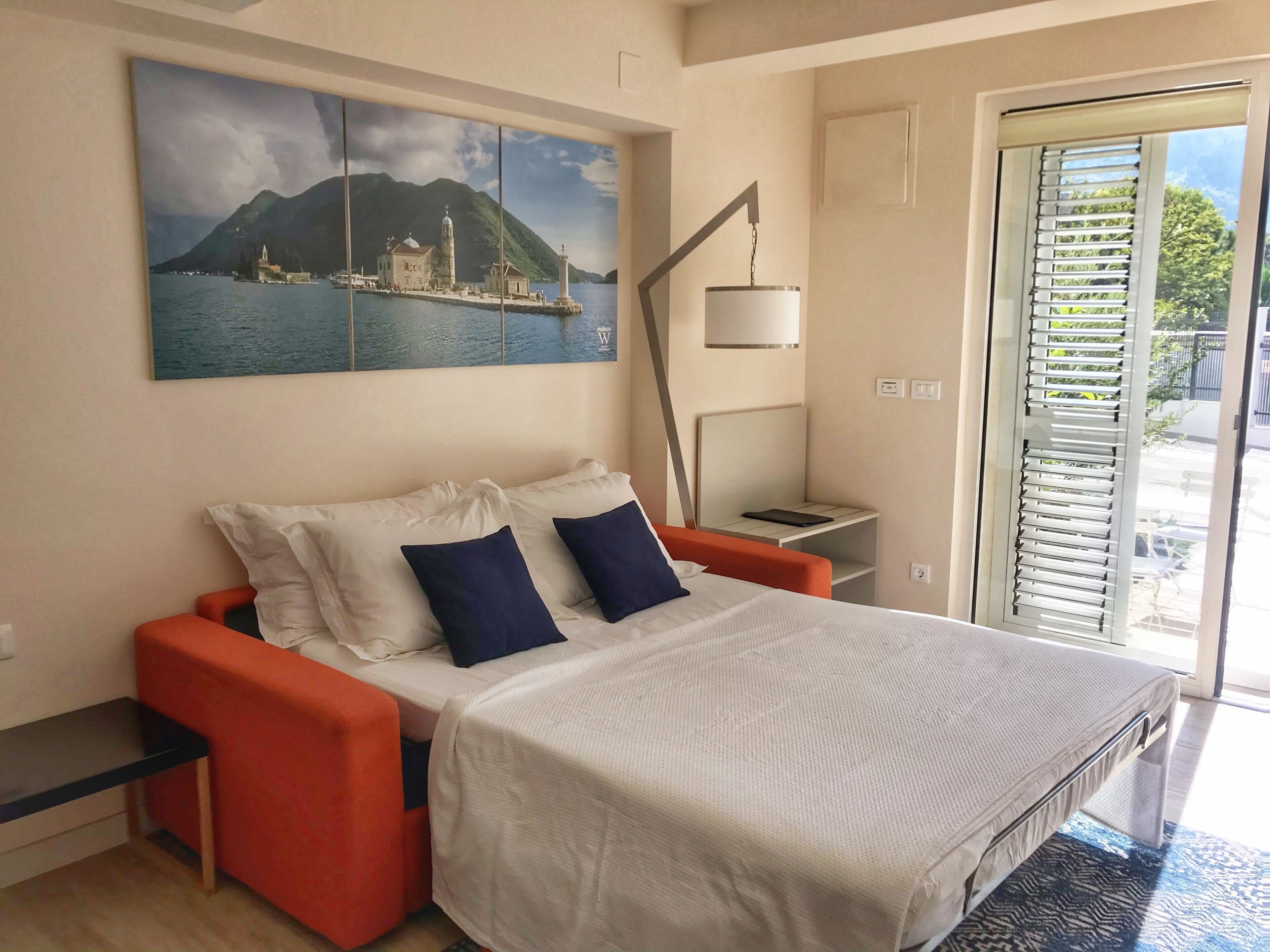 A bedroom with a bed, a nightstand, a lamp, and a painting of a coastal scene.