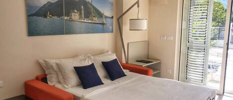 A bedroom with a bed, a nightstand, a lamp, and a painting of a coastal scene.