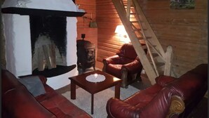 A cozy log cabin interior with a fireplace, leather furniture, a ladder, and rustic decor.