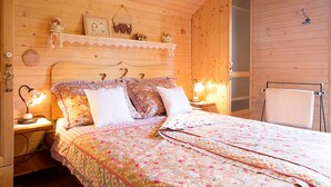 A cozy wooden room with a bed, a nightstand, a shelf with decorative items, and a towel rack.