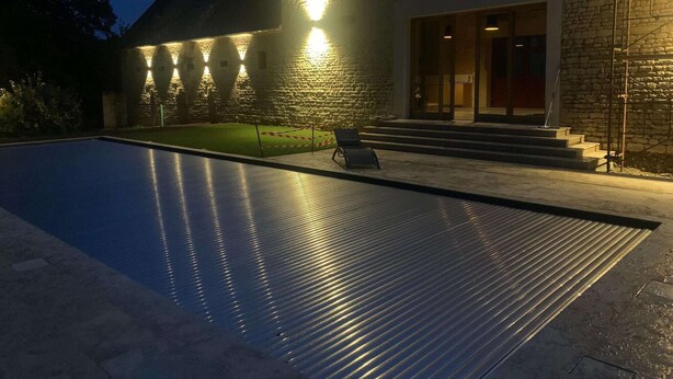 Una piscina con plataforma metálica, un edificio de piedra con fachada de piedra y una escalera que lleva a una puerta.