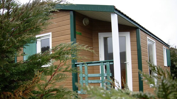 A small wooden cabin with a green door and window shutters, surrounded by trees.