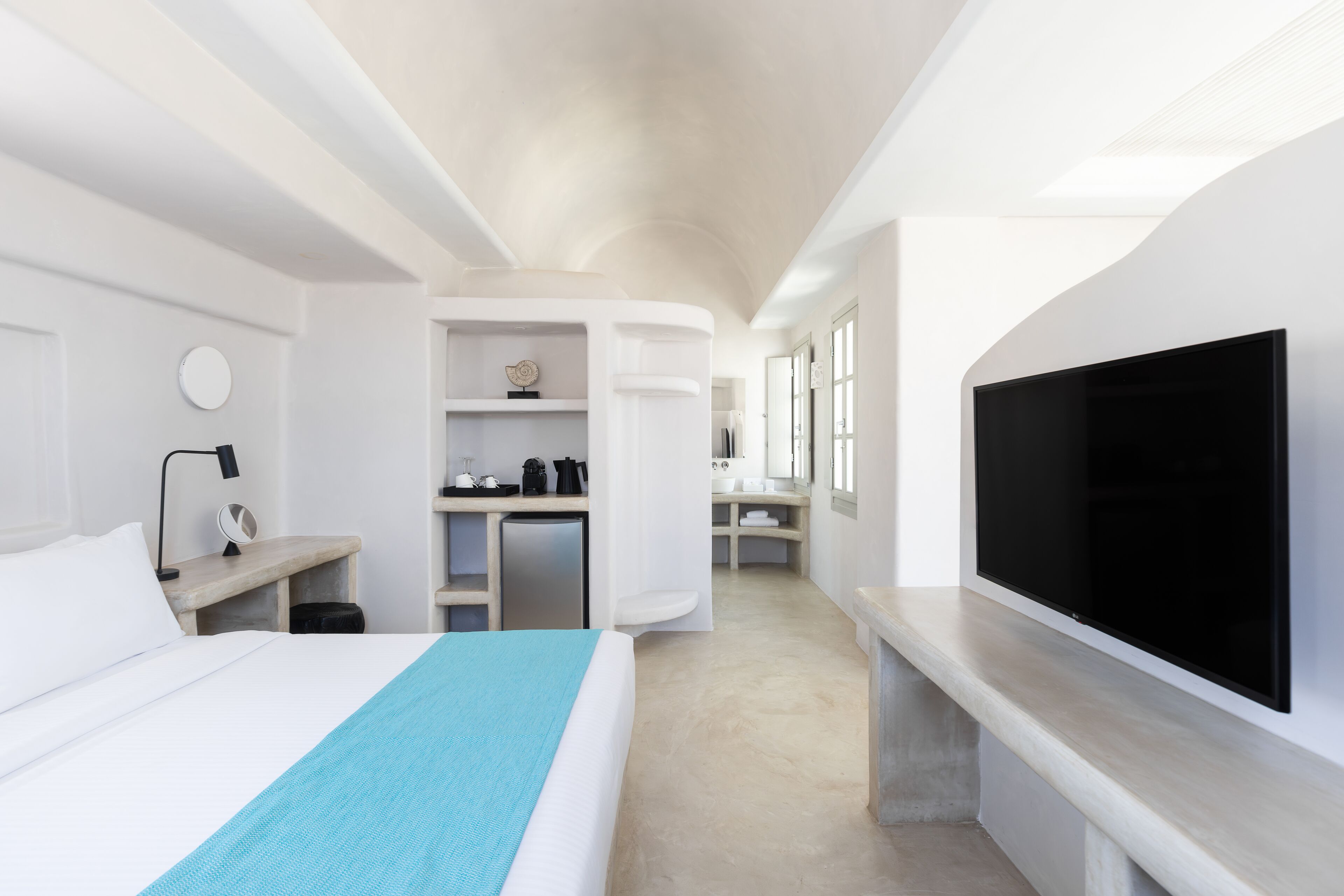 Ein modernes Hotelzimmer mit Bett, Fernseher, Schreibtisch und einem durch eine offene Tür einsehbarer Badezimmer.