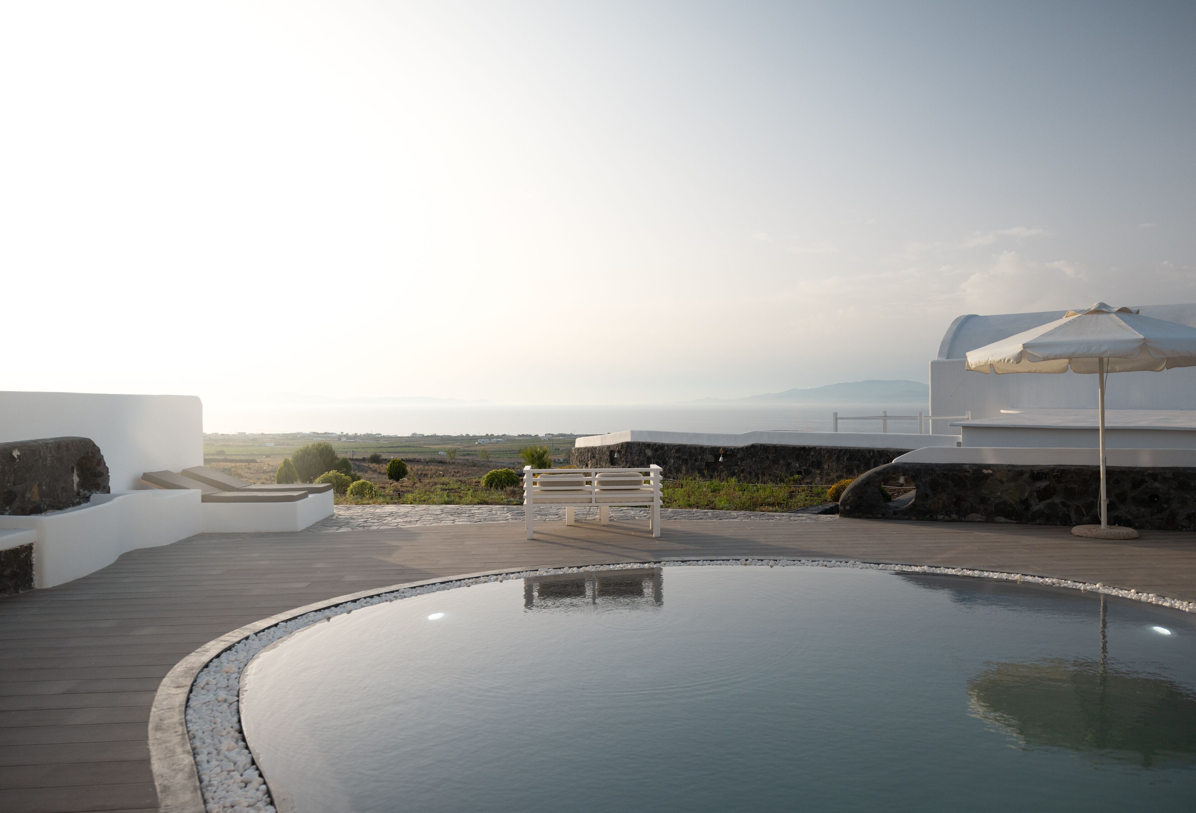 Ein Poolbereich mit einer Bank und einem Sonnenschirm, umgeben von einer modernen Architektur.