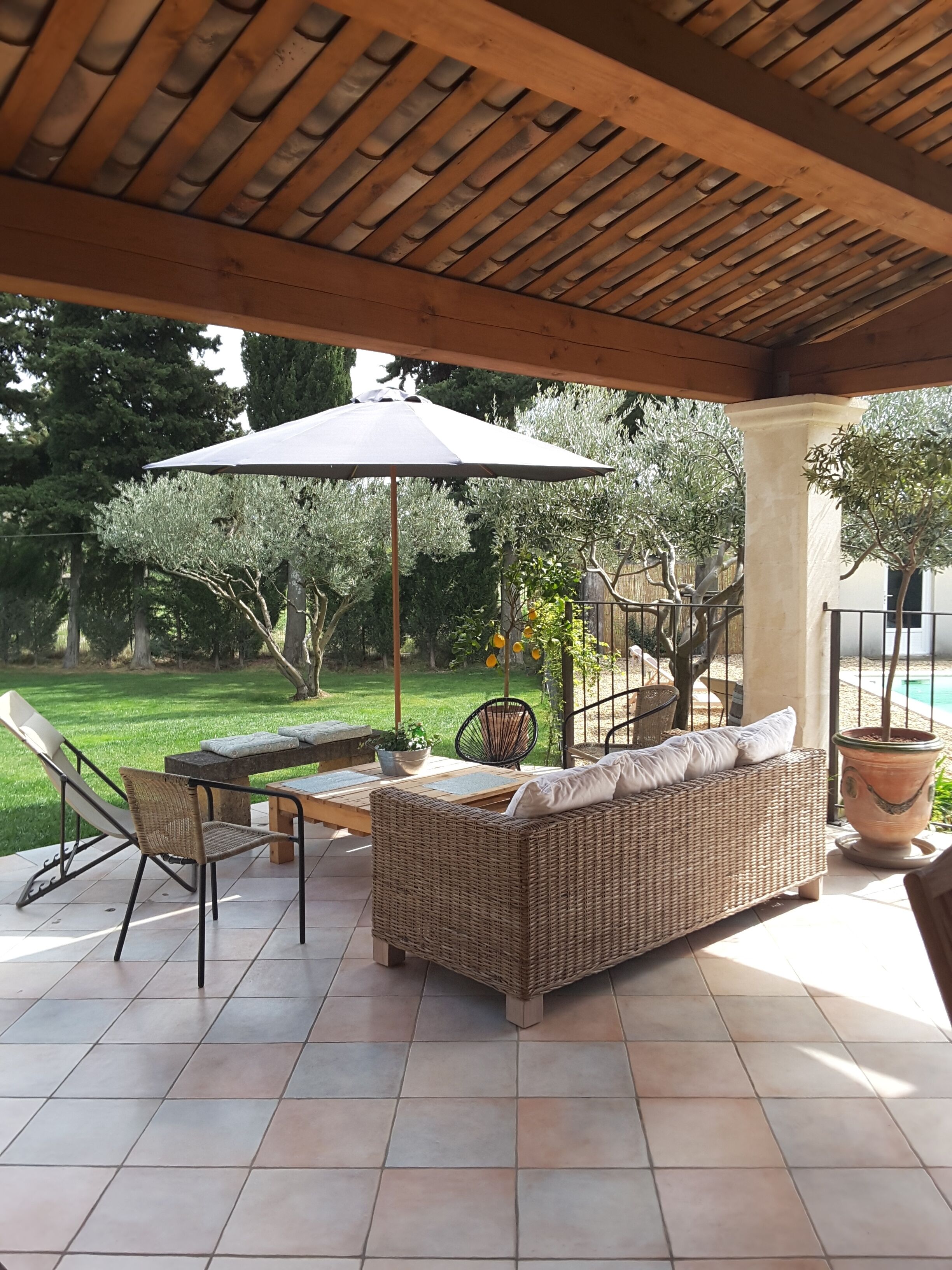 Une terrasse extérieure avec un canapé en osier, une table et des chaises. Un grand parasol offre de l’ombre.
