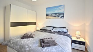 Et soveværelse med seng, natbord, lampe, et billede og et skab.