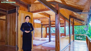 A wooden interior with a person standing by a door, a bed, and a balcony with a view.
