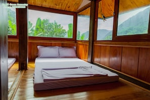 Una habitación de madera con una cama, ventanas amplias y vistas a zonas verdes.