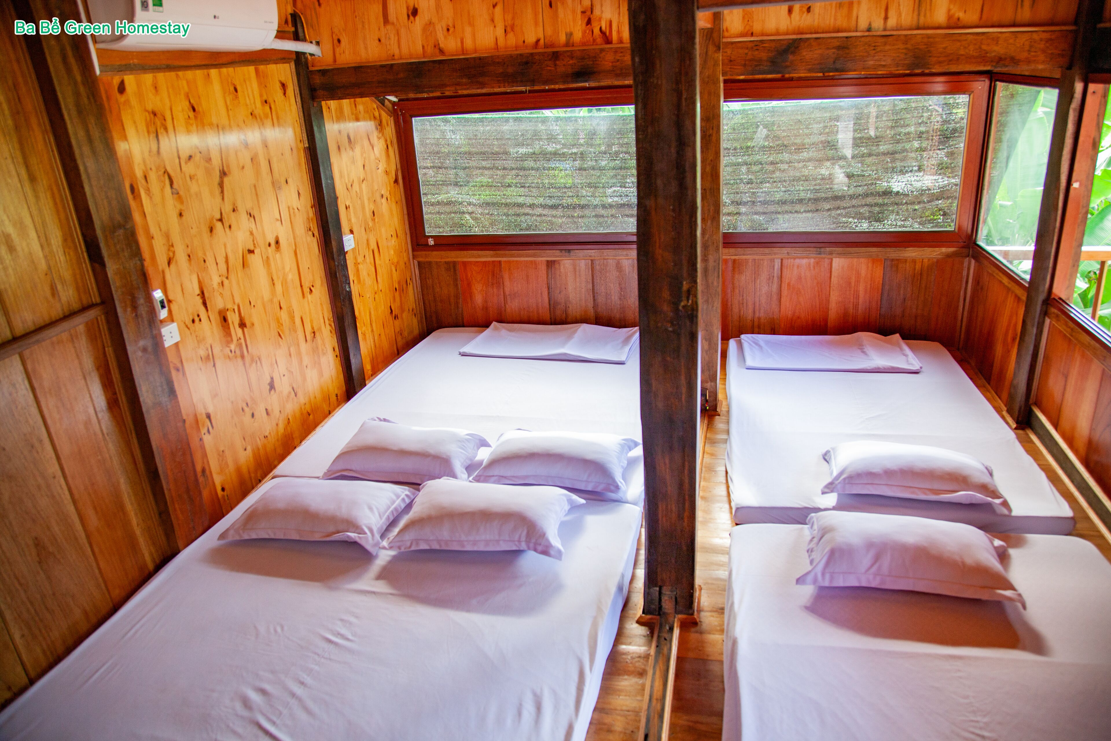 A cabin with two beds, each with white linens and pillows, wooden walls, and a window with a view of greenery.