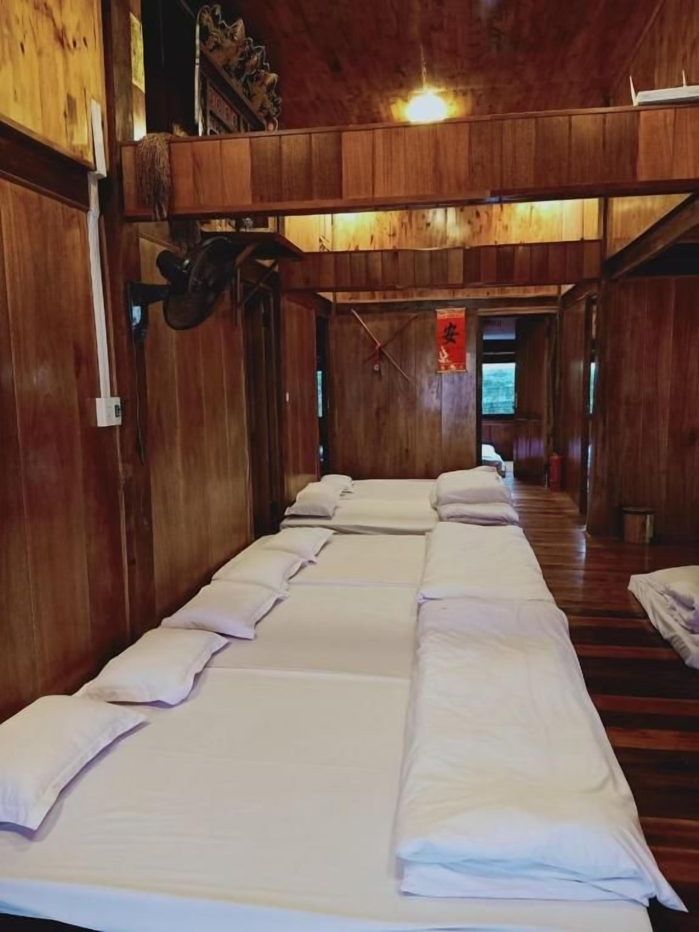 A row of neatly made beds with white linens in a wooden room with a sloped ceiling.