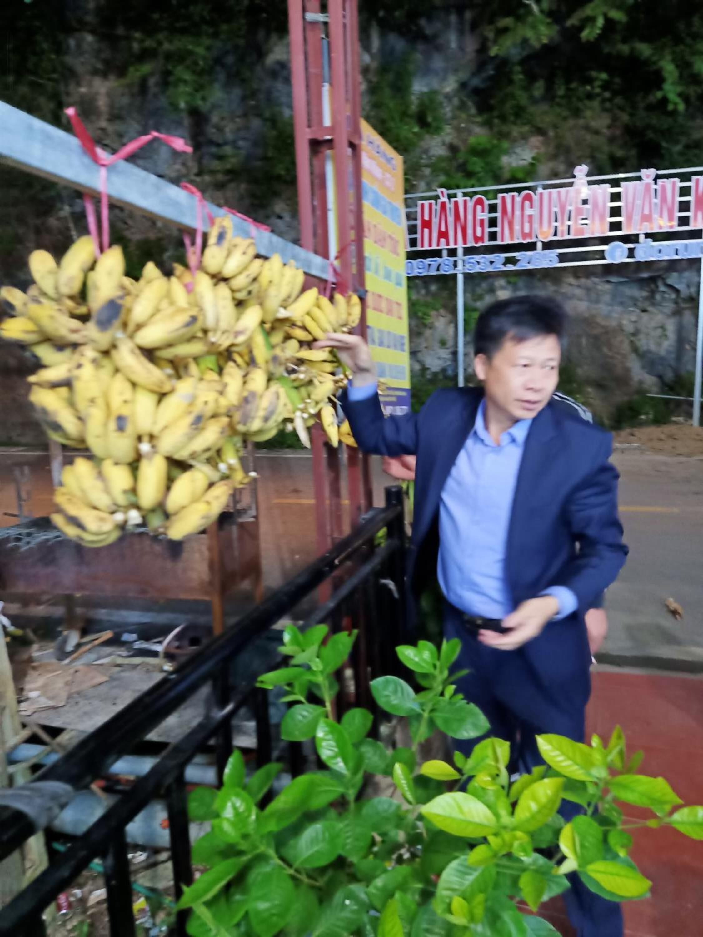 A man holding a bunch of bananas in front of a sign with text.