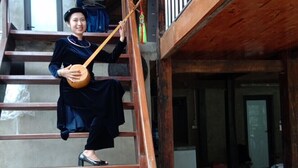 A person sitting on a wooden staircase inside a building with a concrete floor and a metal railing.