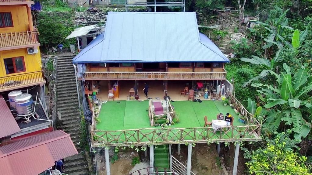 A two-story building with a blue roof, a green outdoor area with a table and chairs, and a staircase leading to the upper level.
