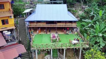 A two-story building with a blue roof, a green outdoor area with a table and chairs, and a staircase leading to the upper level.