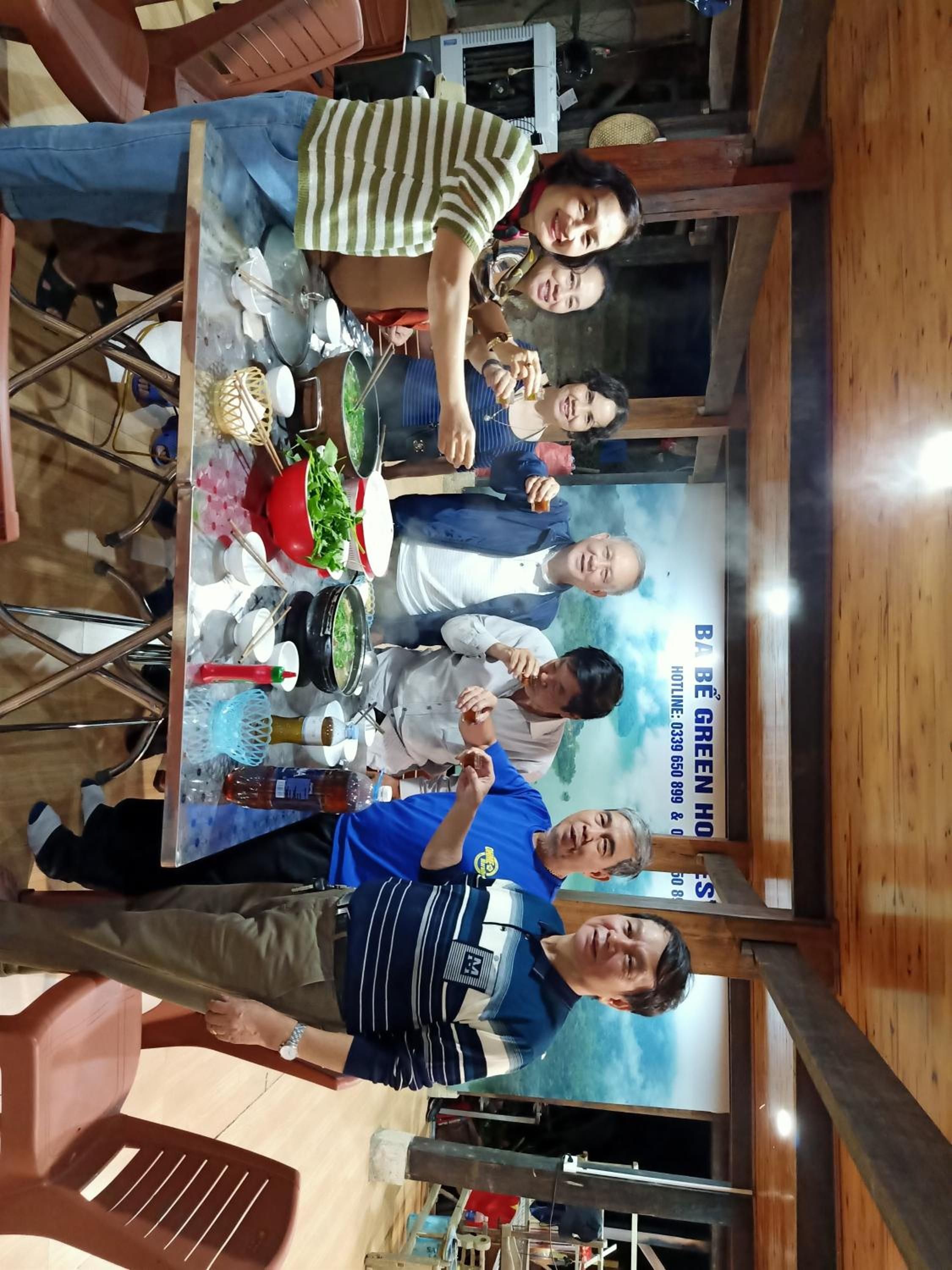A group of people seated around a table with a variety of dishes and utensils, indicating a dining setting.