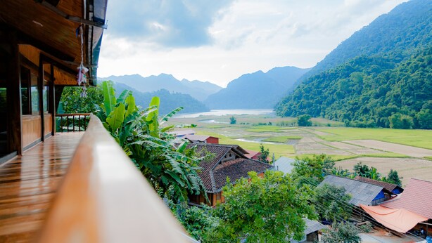 A view from a balcony overlooking a river, with mountains in the background and a wooden building with a tiled roof in the foreground.