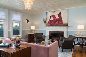 A living room with a fireplace, two armchairs, a sofa, and a table with a vase of flowers. - Atlantean Cottage (Bar Harbor)
