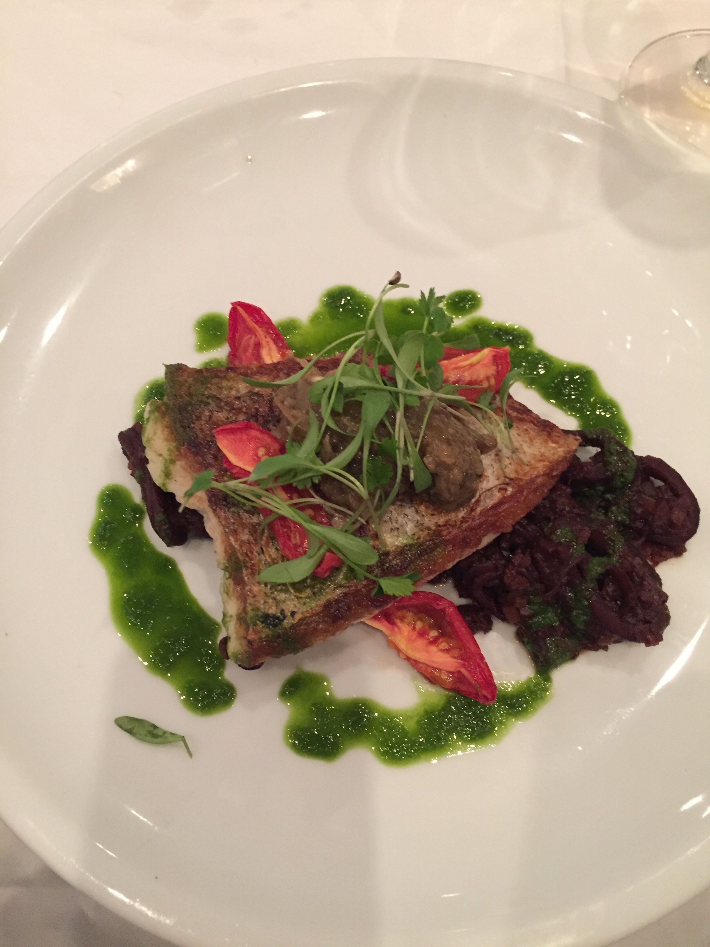 Un piatto bianco con un pezzo di pesce alla griglia, verdure verdi e fette di pomodoro rosso.