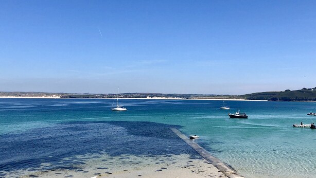A coastal scene with clear blue waters, boats, and a sandy beach.