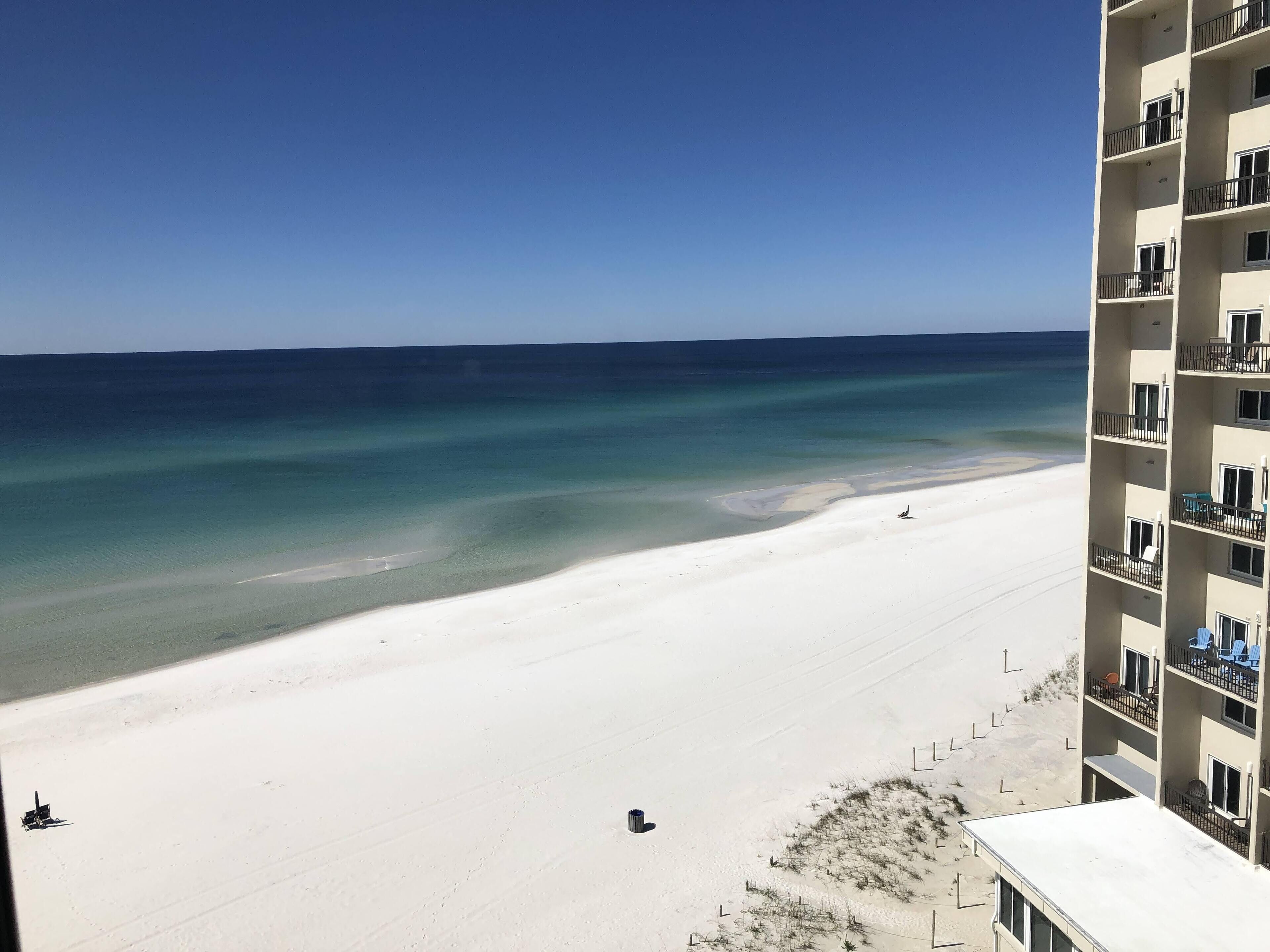 A beach view from a high-rise building with balconies overlooking a sandy beach and clear blue waters.