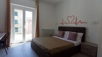 Ein Schlafzimmer mit einem Bett, einem Nachttisch, einem Schreibtisch und Blick ins Freie durch eine Schiebetür.
