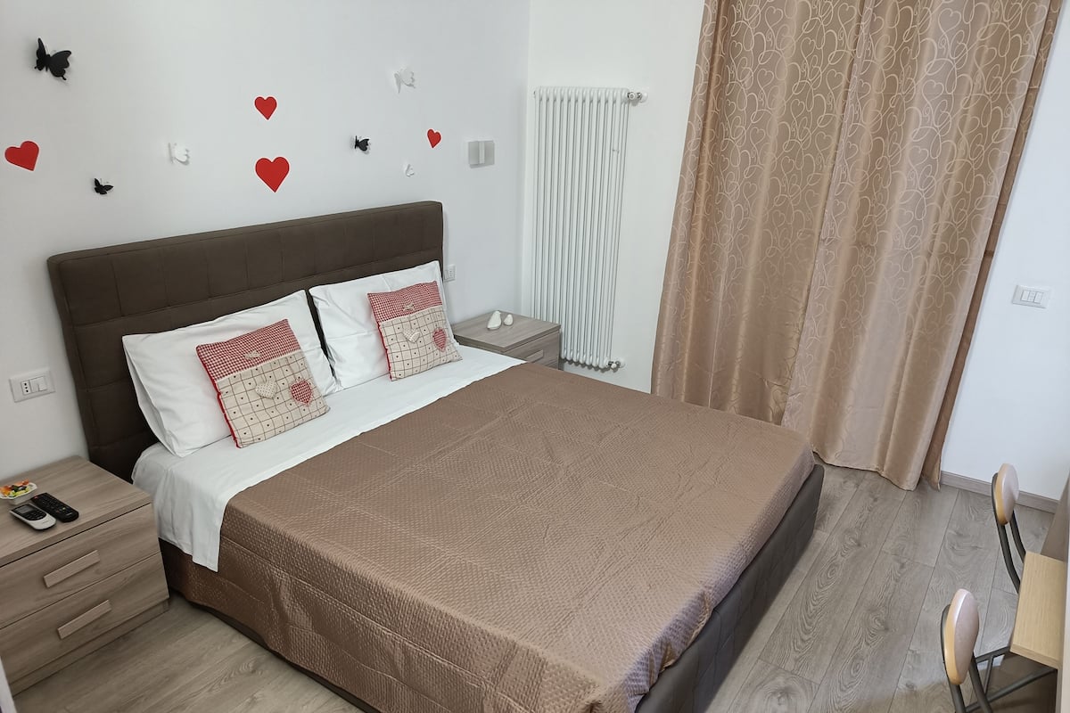 Una cama bien tendida con un edredón marrón, almohadas blancas con diseños rojos y un cabecero marrón.