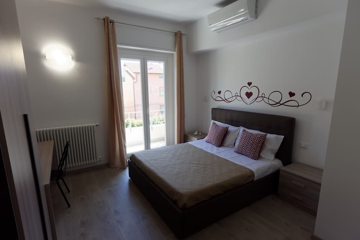 Un dormitorio con cama, radiador, ventana con cortinas y una decoración en la pared.