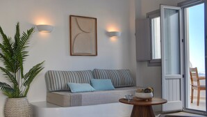 Een moderne woonkamer met een bank, twee kussens, een bijzettafeltje, een potplant en een schilderij aan de muur.