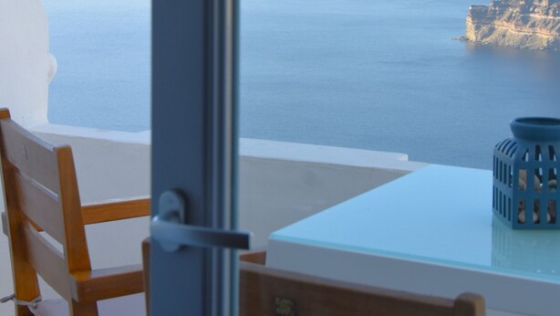 Een kamer met uitzicht op zee en kliffen, een houten stoel en een glazen tafel.