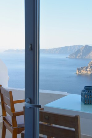 A room with a view of the sea and cliffs, a wooden chair, and a glass table. - Caldera St. G | Stunning Caldera Views from Your Private Balcony (Thera)