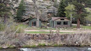 A rustic cabin with a stone foundation, a small porch, and a picnic table. - Great Getaway on the Big Thompson very near Estes & Rocky Mt. Nat'l Park (Drake)