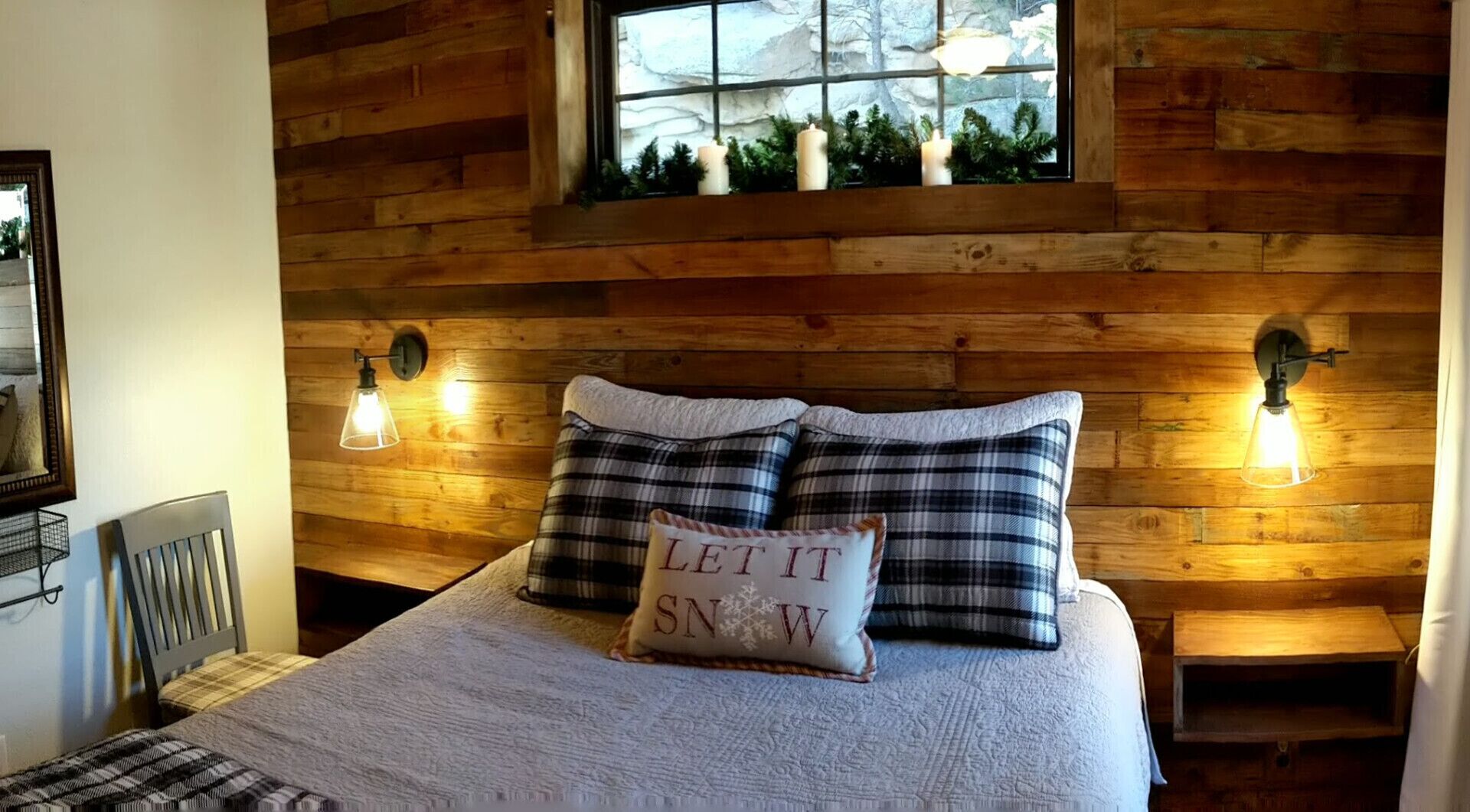 Um quarto aconchegante com cabeceira de madeira, duas luminárias de apoio e uma janela com vista para árvores e velas.