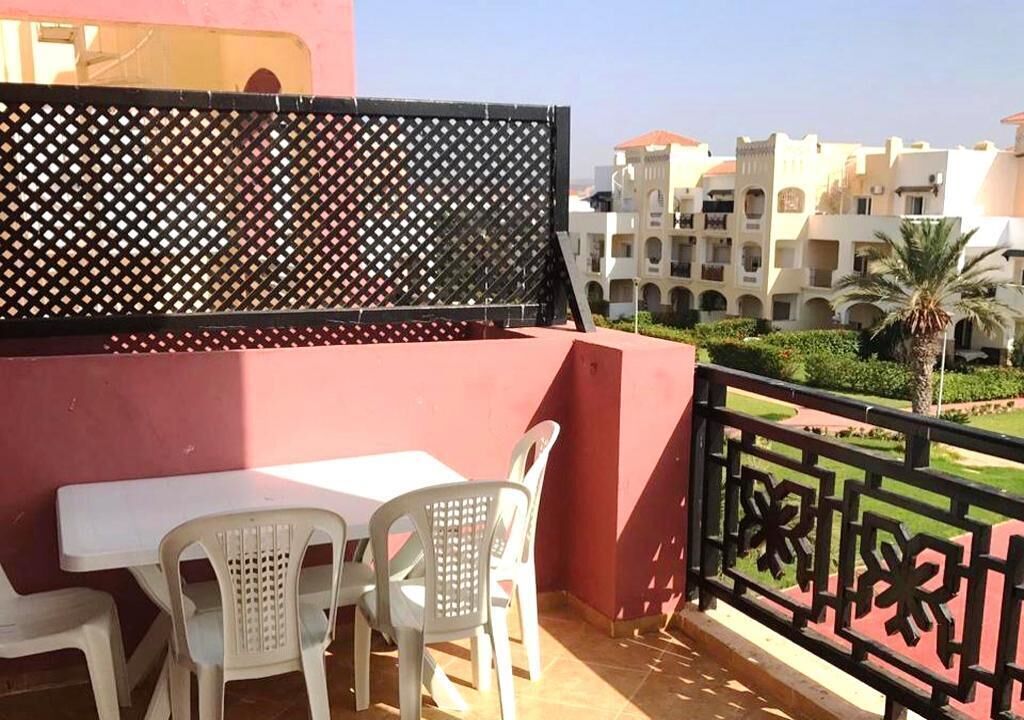 A balcony with a table and chairs, a decorative fence, and a view of a building complex.
