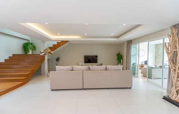 Una sala de estar moderna con una escalera de madera, un sofá color beige y un ventanal con cortinas.