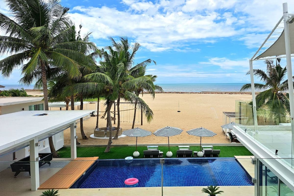 Una piscina con vistas a la playa, sillas de descanso y palmeras.