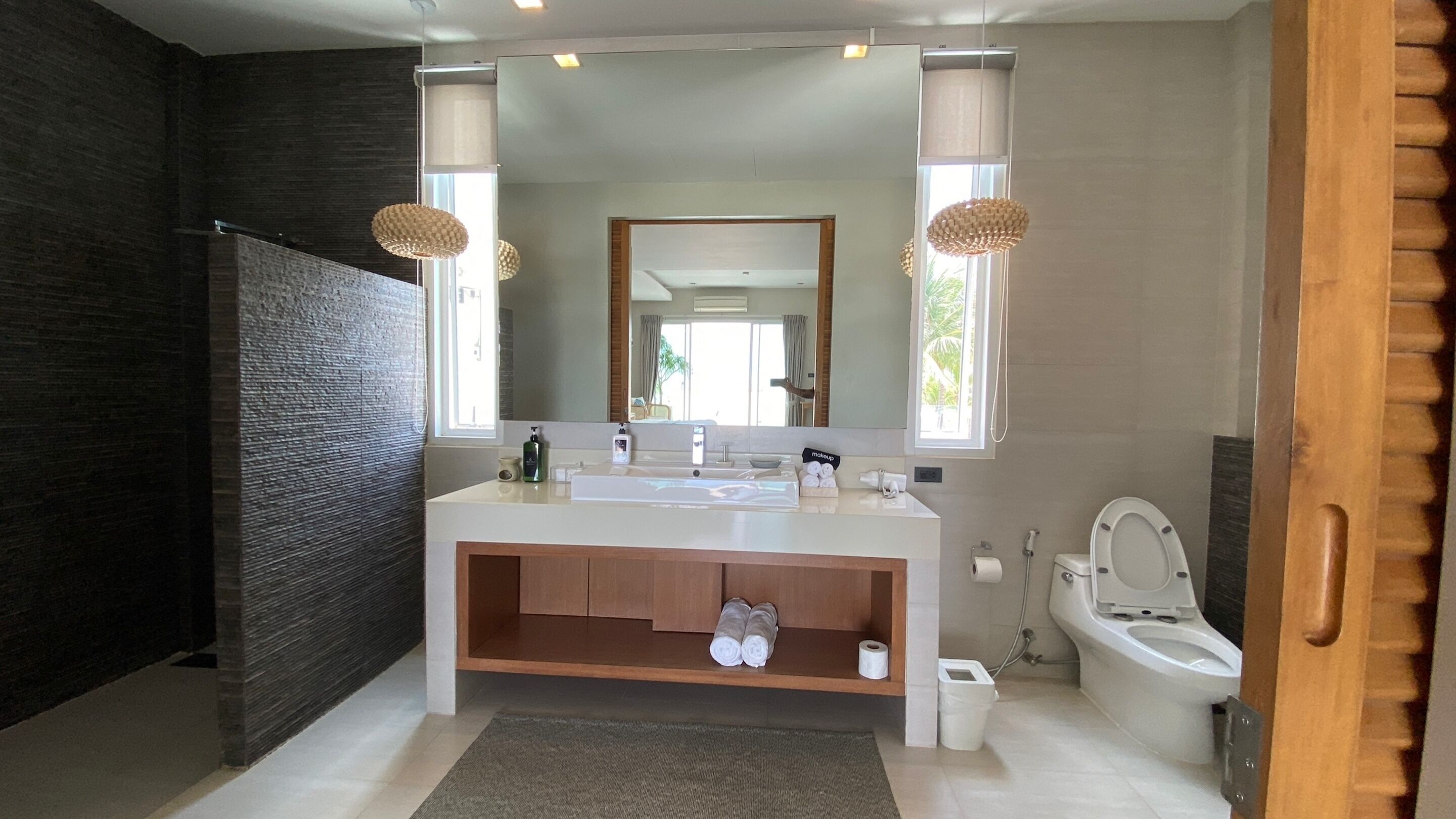 A modern bathroom with a large mirror, a white sink, a wooden vanity, and a toilet.