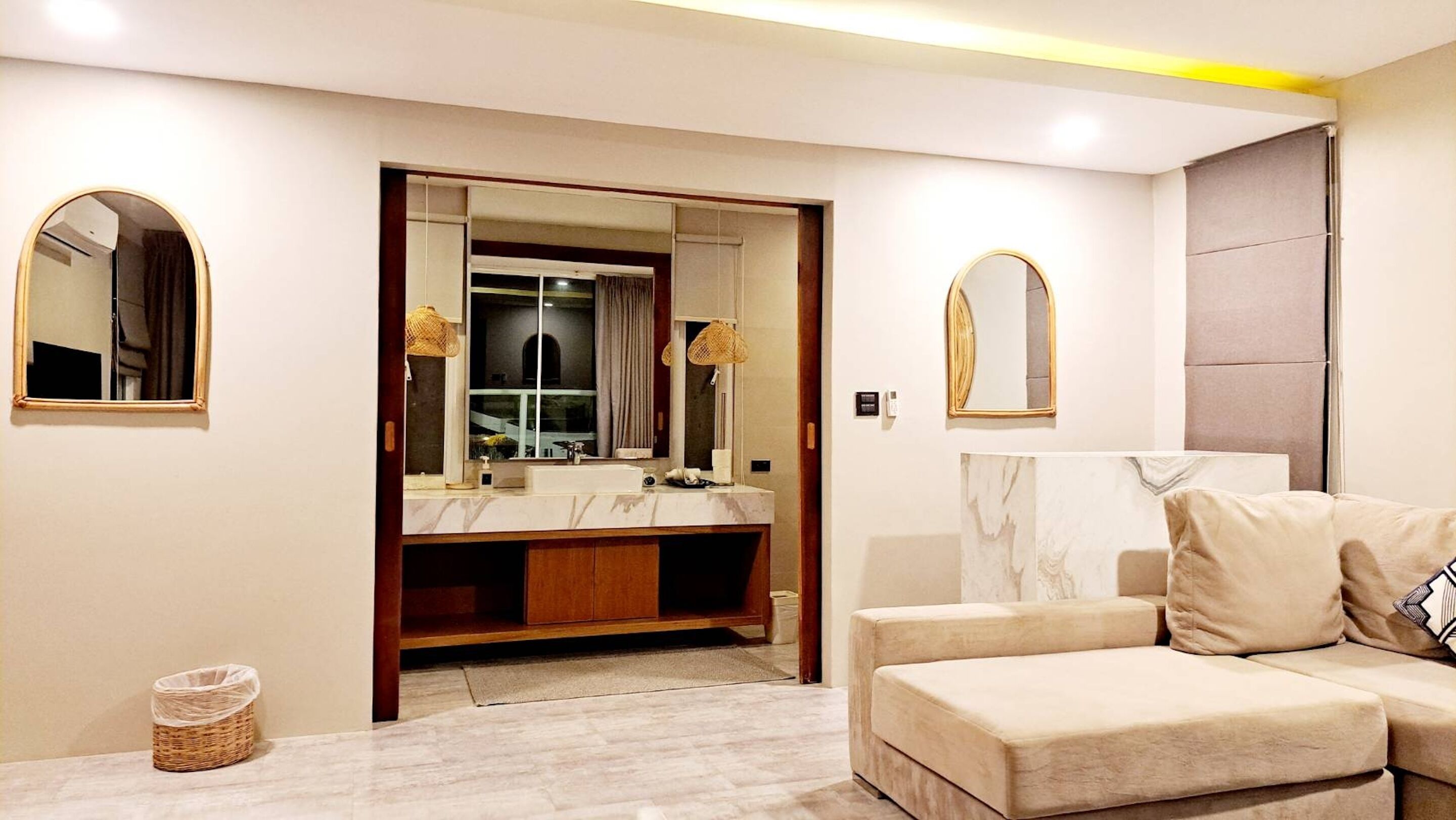A modern bathroom with a vanity, mirrors, and a sofa in the adjacent living area.
