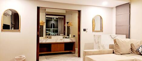 A modern bathroom with a vanity, mirrors, and a sofa in the adjacent living area.